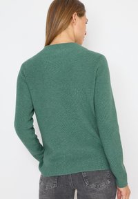 Pull verte à côtes avec des manches longues et un col rond, présentant un motif de tricot texturé et un ourlet droit.