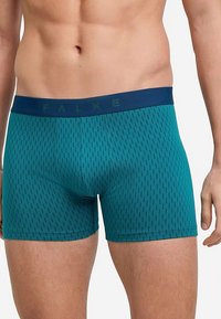 Herren-Boxershorts in Petrol mit gemustertem Stoff und einem blauen elastischen Bund mit "FALKE" Branding, figurbetonter Schnitt.