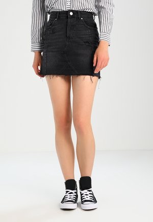Personne portant une mini-jupe en denim noir usé, une chemise à rayures boutonnée, et des baskets montantes noires avec des lacets blancs.