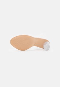 Chaussure à talon haut transparent unique avec semelle beige texturée et talon bloc transparent sur fond blanc.