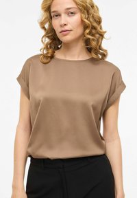 Blouse en satin marron avec manches courtes retroussées, encolure ronde et coupe ample, associée à un pantalon noir. Texture lisse, design minimaliste.