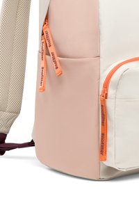 Roh žltého batohu s béžovým sieťovým popruhom, ružovými a bielymi textíliami a oranžovými zipsami označenými "#nofilter".