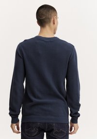 Pull à manches longues bleu foncé avec un tricot texturé, encolure ronde et poignets côtelés. Présente une finition lisse et une coupe décontractée.