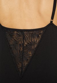 Abito nero con un inserto in pizzo triangolare sulla schiena, che evidenzia motivi floreali intricati. Tessuto morbido e spalline regolabili.