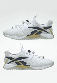 Chaussures de sport blanches avec des bandes latérales abstraites noires et dorées, des sangles élastiques et des semelles rembourrées, vues de côté et de l'intérieur.