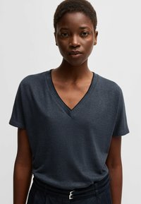 Dark grey V-neck t-shirt with short sleeves, made from soft, textured fabric. Paired with a black waistband featuring a silver buckle detail.