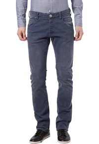 Mężczyzna w wyblakłych niebieskich dżinsach, czarnych trampkach i jasnoszarej koszuli w kratkę z długimi rękawami, stojący z relaksowanymi rękami.