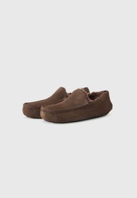 Bruine suede instappers met een faux fur voering, ronde neus en decoratieve stiksels op de bovenkant. Laag profiel zool voor comfort.