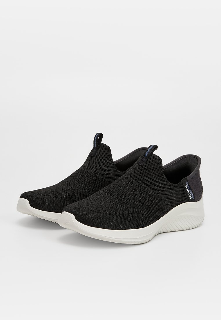Svarta slip-on skor med en texturerad stickad ovandel, vit sula och en subtil logotyp på hälen. Lättviktig design för komfort.