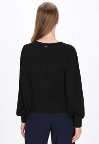 Zwarte blouse met lange, geplooide mouwen, een ronde halslijn en een discreet sluiting aan de achterkant met een kleine metalen accent. Gladde textuur.