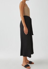 Jupe midi noire plissée avec une ceinture à nouer, assortie à des sandales plates en tressé. Le haut est un débardeur ajusté de couleur neutre. Design simple et minimaliste.