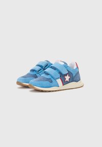 Des baskets en suède bleu avec deux bandes Velcro, une rayure blanche et un accent en étoile rouge sur le côté. Semelle en caoutchouc avec une texture antidérapante.