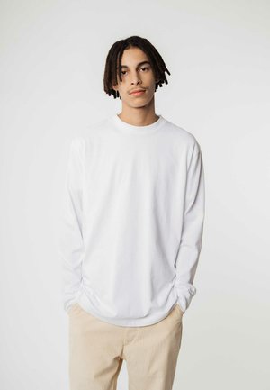 Witte langemouw t-shirt met een ronde hals, met een ontspannen pasvorm en zachte textuur, gecombineerd met lichtbeige corduroy broek.