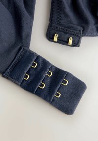 Tissu bleu marine au toucher lisse, avec une fermeture crochet et œillet et quatre crochets en métal doré pour un ajustement réglable.