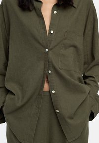 Oliwkowa koszula z guzikami, z kieszenią; wykonana z teksturowanej tkaniny; posiada perłowe guziki i luźny krój.