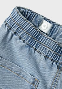 Pantalon en denim bleu clair avec une taille élastique, doté d'un petit bouton blanc et d'une seule poche arrière avec des coutures visibles.