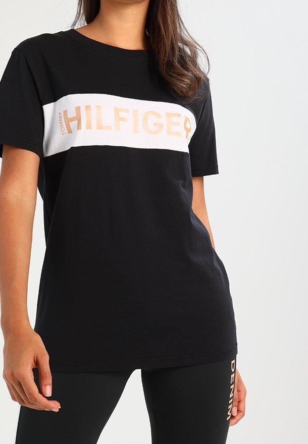 Černé bavlněné tričko s bílým a zlatým logem "TOMMY HILFIGER" na hrudi. Krátké rukávy a uvolněný střih.