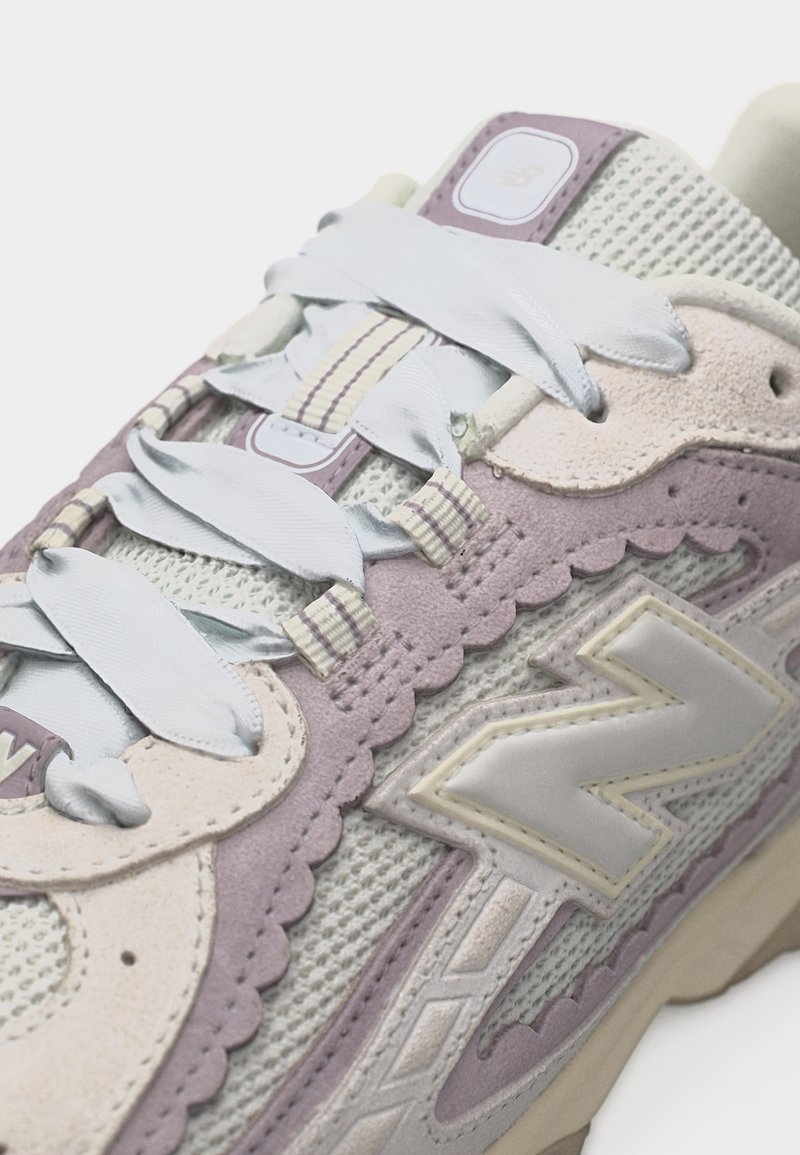 Zapatilla de malla y ante en beige y lavanda con cordones blancos y un gran logo "N" en el lateral.