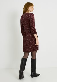 Vestido de manga corta en burdeos con estampado floral, cintura fruncida y falda acampanada; combinado con botas de piel negras hasta la rodilla.