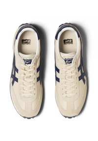 Sneakers beige con accenti blu navy, caratterizzati da un mix di materiali lisci e testurizzati, design classico con lacci e suola in gomma.