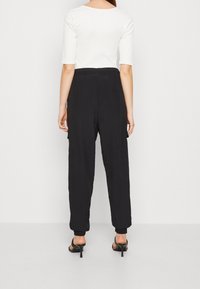 Svarta, löst sittande byxor med en texturerad tyg, som har en elastisk midja och manschetter vid anklarna. Bärs med en vit, figurnära topp.