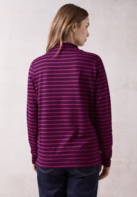 Maglietta a maniche lunghe a righe viola con strisce magenta, realizzata in un tessuto morbido. Presenta un colletto alto e una vestibilità comoda.