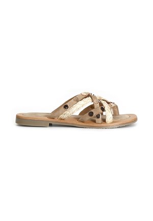 Sandalia plana beige con tiras trenzadas y de ante que se cruzan sobre el pie, decorada con tachuelas metálicas redondas y una suela delgada de goma.