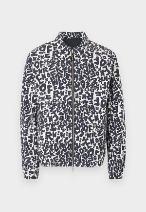 Fehér cipzáros dzseki fekete absztrakt betűmintával, hegyes gallérral, elasztikus mandzsettákkal és két első zsebbel, egyszínű háttéren.