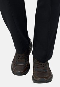 Des chaussures de sport marron avec des accents et des lacets noirs, associées à un pantalon droit noir. Les chaussures présentent une surface texturée et une semelle en caoutchouc.