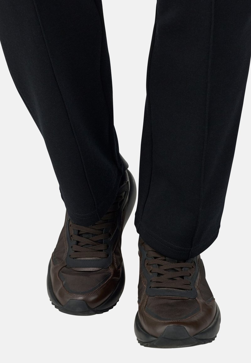 Des chaussures de sport marron avec des accents et des lacets noirs, associées à un pantalon droit noir. Les chaussures présentent une surface texturée et une semelle en caoutchouc.
