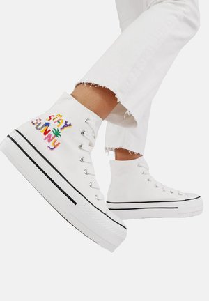 Sneakers alte bianche in tela con suola nera. Presentano testo ricamato multicolore "Stay Sunny" e elementi decorativi.