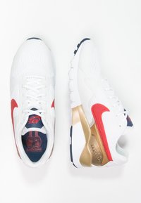 Baskets de sport blanches avec des accents rouges et dorés. Tige texturée, bout rond et semelle rembourrée. Présence du logo Nike sur le côté.