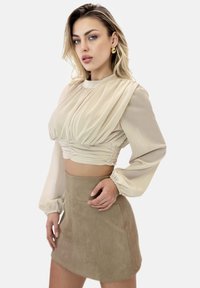 Top beige corto con design plissettato e maniche lunghe, abbinato a una gonna mini in suede taupe, di texture liscia e silhouette aderente.