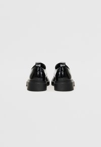 Chaussures en cuir verni noir au design épuré, avec un bout arrondi et de grosses semelles en caoutchouc noir. Comprend des pattes de talon au-dessus du dos.