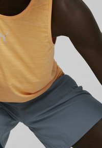 Débardeur de sport orange à finition texturée avec logo PUMA argenté, accompagné de shorts gris foncé. Accent sur un design respirant et sportif.