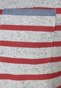 Szara koszulka z krótkim rękawem z czerwonymi poziomymi paskami i niebieską kieszenią. Jasne kropeczki na tkaninie dodają faktury projektowi.