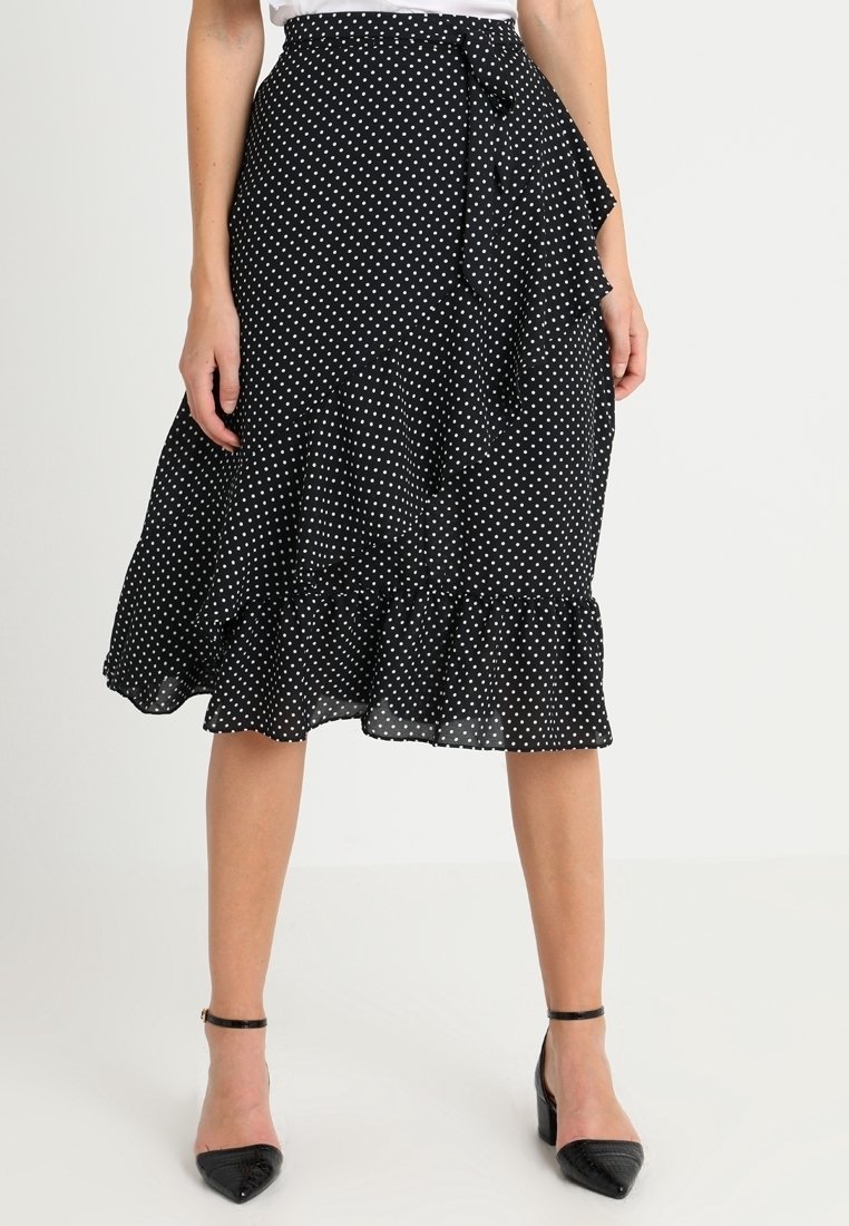 Černá sukně s puntíky z lehké tkaniny, má volánkový lem a zavazovací detail v pase. Stylizováno s černými lodičkami na podpatku.