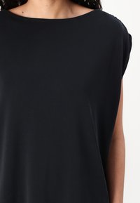 Top scurt negru, cu mâneci scurte, fabricat dintr-un material ușor, cu un decolteu larg și o croială lejeră, având o textură moale și un design minimalist.