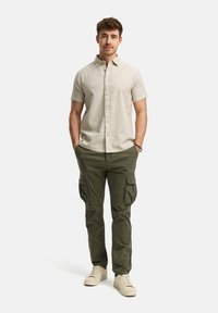 Camisa de manga corta color beige claro con una textura sutil, combinada con pantalones cargo verdes oliva que tienen múltiples bolsillos. Zapatillas color crema completan el look.