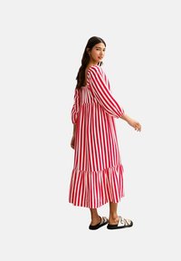 Vestido de rayas rojas y blancas, con mangas largas, falda de capas y cintura fruncida. Llevado con sandalias negras. Tela suave y ligera.