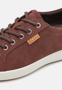 Baskets en daim marron avec bout rond, œillets en métal et lacets marron. Présente une petite étiquette logo Ecco beige sur le côté et une semelle en caoutchouc blanc.