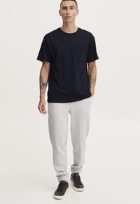 Tricou din bumbac bleu închis cu un buzunar pe piept, asortat cu pantaloni de trening gri deschis. Adidași negri cu o talpă albă completează ținuta.
