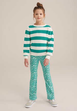 Suéter de punto a rayas verdes y blancas combinado con pantalones acampanados de flores verdes y zapatillas grises, todo sobre un fondo neutro.