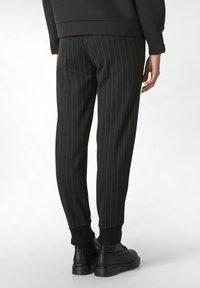 Zwarte pinstripe broek met groene strepen, voorzien van geribbelde enkelmanchetten, een slanke silhouet en een gladde stoftextuur.