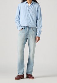 Ljusblå långärmad skjorta med knäppning fram och bröstficka, tillsammans med ljusblå raka jeans och vinröda båtsskor.