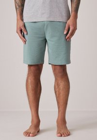 Pantalones cortos verde menta fabricados en un tejido suave, con un diseño simple, corte recto y bordes dobladillados, combinados con una camiseta gris.