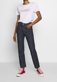 Camiseta blanca con la palabra "FEMME" en letras rojas, combinada con jeans de tiro alto en azul oscuro y zapatillas rojas de caña alta.
