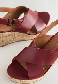 Burgundin väriset nahkaiset slingback-sandaalit, joissa on korkkipohja, ristikkäiset hihnat ja hopeinen solkiyksityiskohta. Silkkinen pinta ja pyöristetty varvas.
