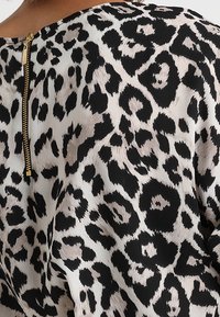 Blůza s leopardím potiskem, vyrobená z hladké látky; má zlatý zip na zadní straně a volný, kulatý výstřih.