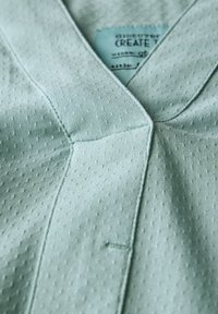 Tissu vert clair avec un motif texturé en points. Présente une encolure en V et des coutures visibles. L'étiquette indique "découvrir, CRÉER."